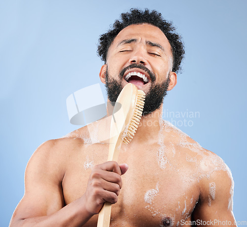 Image of Shower, brush and man singing in studio for cleaning, wellness or morning routine on blue background. Bathroom, karaoke and male model having fun with body scrubber, cosmetics or luxury washing