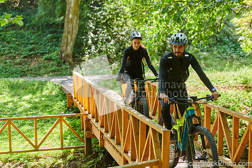 Image of A blissful couple, adorned in professional cycling gear, enjoys a romantic bicycle ride through a park, surrounded by modern natural attractions, radiating love and happiness