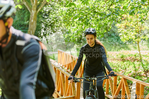 Image of A blissful couple, adorned in professional cycling gear, enjoys a romantic bicycle ride through a park, surrounded by modern natural attractions, radiating love and happiness