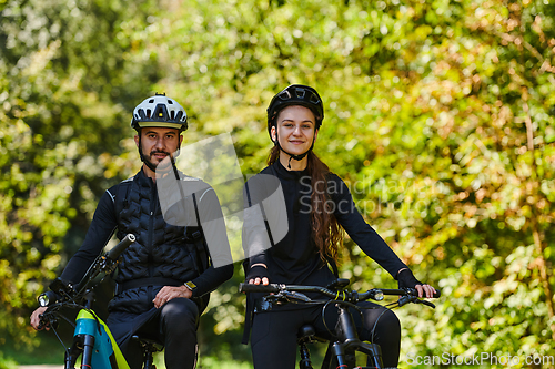 Image of A blissful couple, adorned in professional cycling gear, enjoys a romantic bicycle ride through a park, surrounded by modern natural attractions, radiating love and happiness