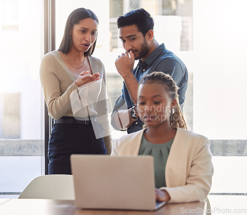 Image of Office bully, woman and working at laptop with coworkers talking in a corporate workplace with gossip. Young black person typing on a computer with internet and joke with staff being mean at desk