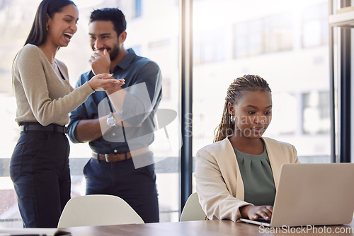 Image of Office bully, woman and working at laptop with coworkers laughing in a corporate workplace about gossip. Young black person typing on a computer with internet and joke with staff being mean at desk