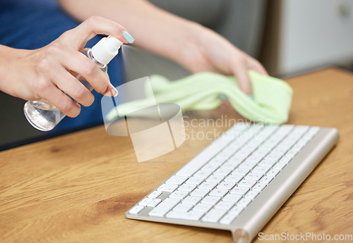 Image of Hands, keyboard and spray bottle with a person cleaning a keyboard on a wooden desk for hygiene. Technology, health and sanitize with an adult wiping a wireless or bluetooth device on a table