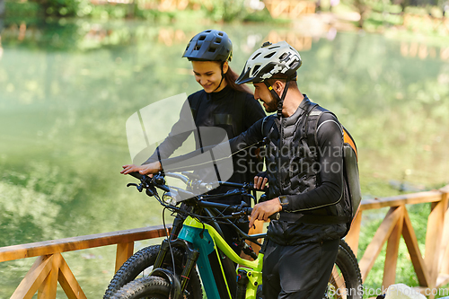 Image of A blissful couple, adorned in professional cycling gear, enjoys a romantic bicycle ride through a park, surrounded by modern natural attractions, radiating love and happiness