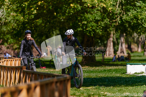 Image of A blissful couple, adorned in professional cycling gear, enjoys a romantic bicycle ride through a park, surrounded by modern natural attractions, radiating love and happiness