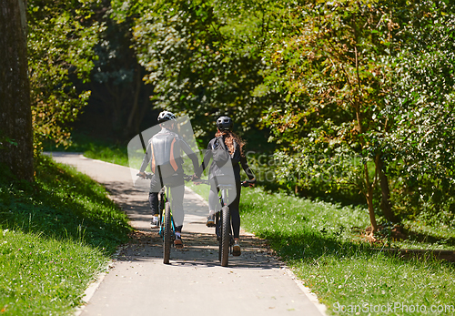 Image of A blissful couple, adorned in professional cycling gear, enjoys a romantic bicycle ride through a park, surrounded by modern natural attractions, radiating love and happiness