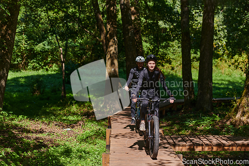 Image of A blissful couple, adorned in professional cycling gear, enjoys a romantic bicycle ride through a park, surrounded by modern natural attractions, radiating love and happiness