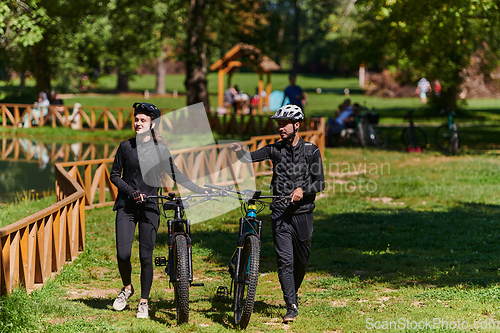 Image of A blissful couple, adorned in professional cycling gear, enjoys a romantic bicycle ride through a park, surrounded by modern natural attractions, radiating love and happiness