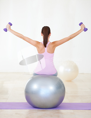 Image of Woman, back and exercise on ball, dumbbells and balance in gym, training and strong muscle in arms. Girl, workout and fitness with pilates, weightlifting and hard work for health, wellness and body