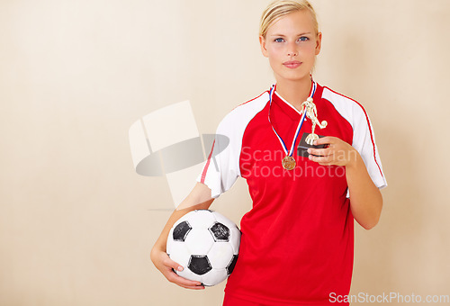 Image of Woman, soccer player and trophy portrait of a winner on a plain background for football achievement. A young female sports person or athlete with a ball and champion medal award for winning a game