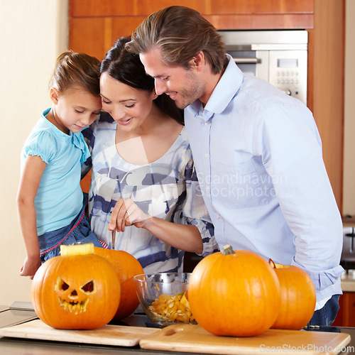 Image of Halloween, pumpkin and a family in the kitchen of their house together for holiday celebration. Creative, smile or happy with a mom, dad and daughter carving a face into a vegetable for decoration