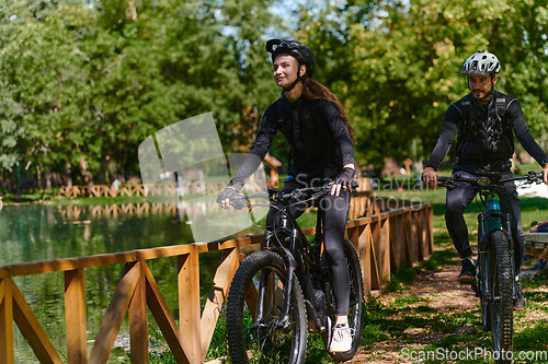 Image of A blissful couple, adorned in professional cycling gear, enjoys a romantic bicycle ride through a park, surrounded by modern natural attractions, radiating love and happiness