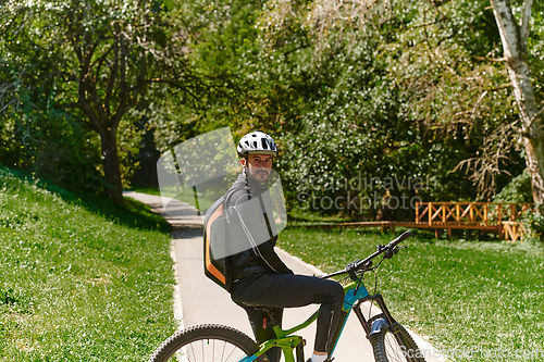 Image of In the radiant glow of a sunny day, a fitness enthusiast, donned in professional gear, pedals through the park on his bicycle, embodying strength and vitality in a dynamic outdoor workout