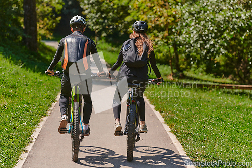 Image of A blissful couple, adorned in professional cycling gear, enjoys a romantic bicycle ride through a park, surrounded by modern natural attractions, radiating love and happiness