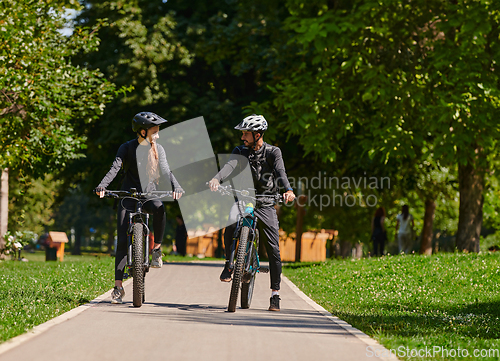 Image of A blissful couple, adorned in professional cycling gear, enjoys a romantic bicycle ride through a park, surrounded by modern natural attractions, radiating love and happiness