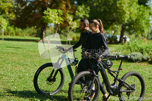 Image of A blissful couple, adorned in professional cycling gear, enjoys a romantic bicycle ride through a park, surrounded by modern natural attractions, radiating love and happiness