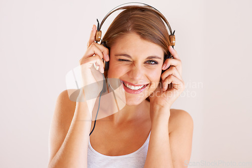 Image of Woman, portrait and wink with headphones in studio for music, audio subscription or streaming multimedia album on white background. Happy model, blink and listening to podcast, hearing sound or radio