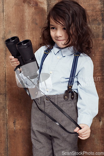 Image of Vintage, child and boy with binoculars or fashion, style and clothes for costume on wood background or studio. Retro, kid and confidence in old fashioned spy aesthetic with shirt and suspenders