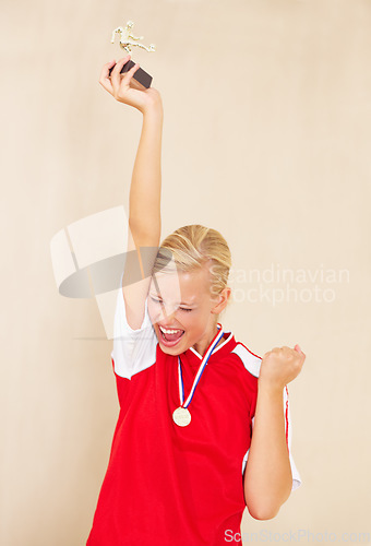 Image of Woman, soccer player and trophy or a winner celebrate on a plain background for football achievement. A young female sports person or athlete with fist and champion medal award for winning a game