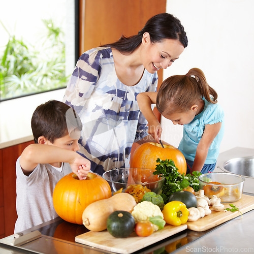 Image of Mother, daughter and son with pumpkins for halloween in the kitchen of their home for holiday celebration. Family, food or tradition and a woman teaching her children how to carve vegetables