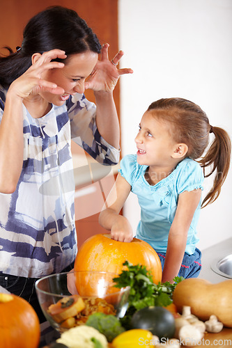 Image of Playful, pumpkin for halloween and a mother with her daughter in the kitchen of their home together for holiday celebration. Smile, happy or funny face with a woman and girl child carving a vegetable