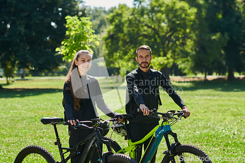 Image of A blissful couple, adorned in professional cycling gear, enjoys a romantic bicycle ride through a park, surrounded by modern natural attractions, radiating love and happiness