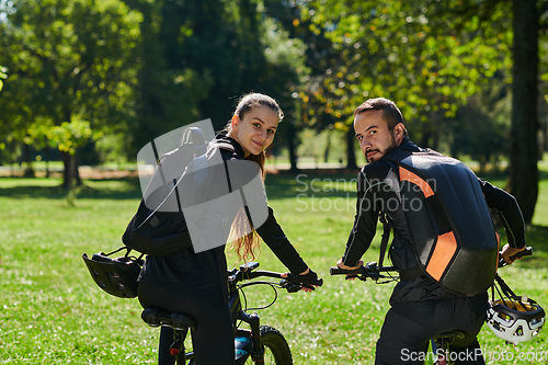 Image of A blissful couple, adorned in professional cycling gear, enjoys a romantic bicycle ride through a park, surrounded by modern natural attractions, radiating love and happiness