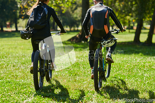 Image of A blissful couple, adorned in professional cycling gear, enjoys a romantic bicycle ride through a park, surrounded by modern natural attractions, radiating love and happiness