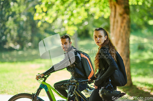 Image of A blissful couple, adorned in professional cycling gear, enjoys a romantic bicycle ride through a park, surrounded by modern natural attractions, radiating love and happiness
