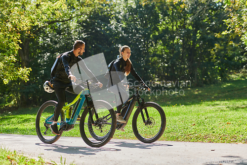 Image of A blissful couple, adorned in professional cycling gear, enjoys a romantic bicycle ride through a park, surrounded by modern natural attractions, radiating love and happiness