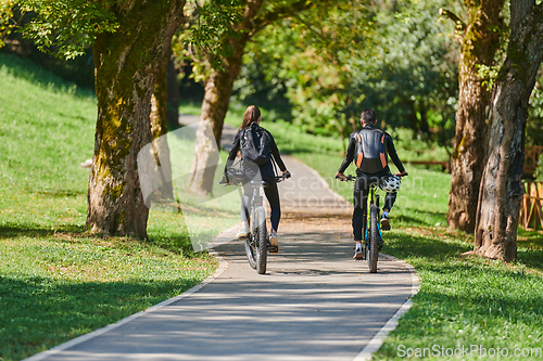 Image of A blissful couple, adorned in professional cycling gear, enjoys a romantic bicycle ride through a park, surrounded by modern natural attractions, radiating love and happiness