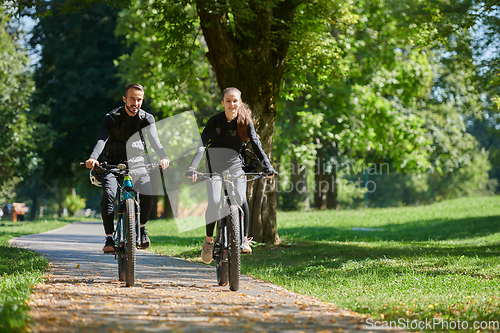 Image of A blissful couple, adorned in professional cycling gear, enjoys a romantic bicycle ride through a park, surrounded by modern natural attractions, radiating love and happiness