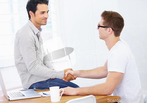 Image of Business men, handshake and agreement at desk in office to offer promotion, support deal and success in creative agency. Team shaking hands for negotiation, onboarding or trust for design partnership