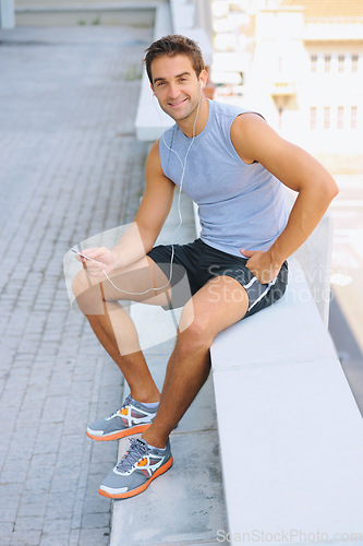 Image of Handsome man, portrait and sitting in fitness on break from exercise, workout or outdoor training on balcony in city. Happy male person smile with earphones listening to music in rest after cardio
