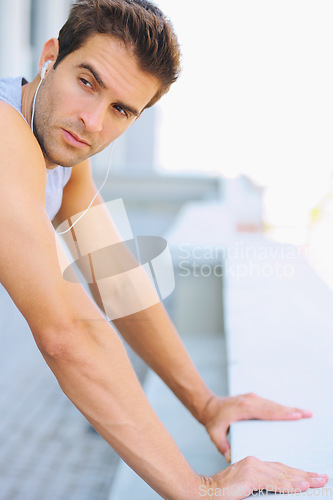 Image of Fitness, earphones and young man athlete by a wall for running listening to music, playlist or album. Sports, workout and male runner training with cardio exercise in street in the city with podcast.