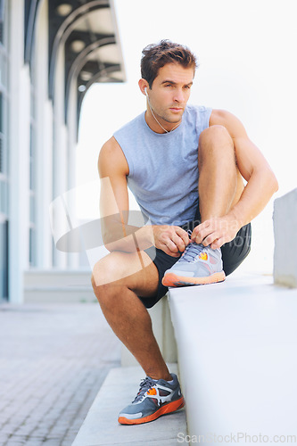 Image of Man, fitness and tying shoes getting ready for workout, exercise or outdoor training with earphones. Active male person or athlete tie shoe on concrete bench in preparation for run or cardio outside