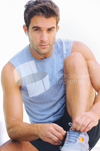 Image of Man, portrait and tying shoes with earphones in fitness for workout or exercise against a white studio background. Active male person or athlete sitting to tie shoe in preparation for cardio training