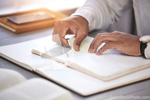 Image of Hands, closeup and sticky note with book on desk for reading, studying and knowledge with planning for analysis. Person, reminder and notebook on table for schedule, project management and process