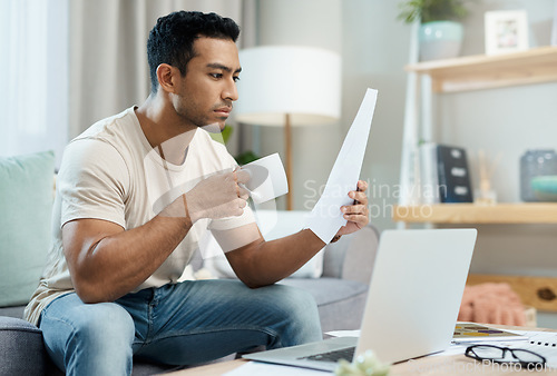 Image of Asian man, laptop and documents with coffee in finance, expenses or checking bills on living room sofa at home. Male person with paperwork, latte or cup of tea reading contract or insurance at house