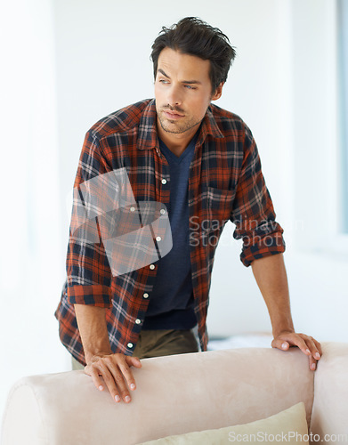 Image of Man, thinking and serious by sofa for ideas, question and contemplating in living room of apartment or home. Person, face or thoughtful or pride by couch in lounge for chill, rest or shirt on weekend