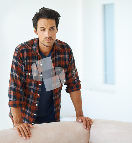 Image of Man, thinking and serious by sofa for idea, question and contemplating in living room of apartment or home. Person, face and thoughtful or calm by couch in lounge for chill, rest and shirt on weekend