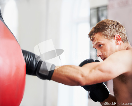 Image of Man, boxing and punching bag at gym for workout, exercise or self defense practice in fighting sport. Active male person or boxer with gloves, energy, indoor training for martial arts at health club