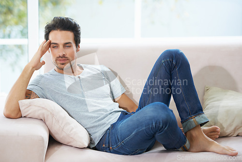 Image of Thinking, depression and man on a sofa with stress, anxiety or broken heart in his home. Sad, crisis or male person in living room overthinking, disaster or lonely, worried or disappointed in a house
