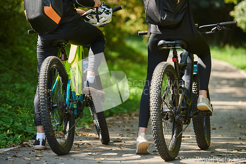 Image of A blissful couple, adorned in professional cycling gear, enjoys a romantic bicycle ride through a park, surrounded by modern natural attractions, radiating love and happiness