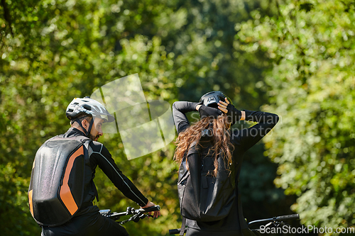 Image of A blissful couple, adorned in professional cycling gear, enjoys a romantic bicycle ride through a park, surrounded by modern natural attractions, radiating love and happiness