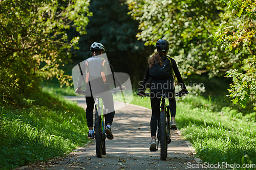 Image of A blissful couple, adorned in professional cycling gear, enjoys a romantic bicycle ride through a park, surrounded by modern natural attractions, radiating love and happiness