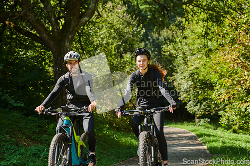 Image of A blissful couple, adorned in professional cycling gear, enjoys a romantic bicycle ride through a park, surrounded by modern natural attractions, radiating love and happiness