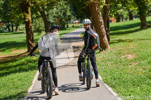 Image of A blissful couple, adorned in professional cycling gear, enjoys a romantic bicycle ride through a park, surrounded by modern natural attractions, radiating love and happiness