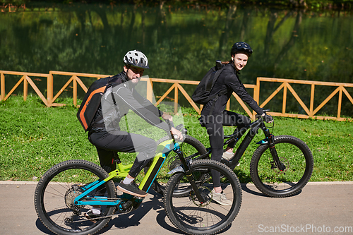 Image of A blissful couple, adorned in professional cycling gear, enjoys a romantic bicycle ride through a park, surrounded by modern natural attractions, radiating love and happiness