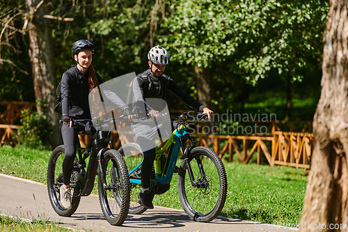 Image of A blissful couple, adorned in professional cycling gear, enjoys a romantic bicycle ride through a park, surrounded by modern natural attractions, radiating love and happiness